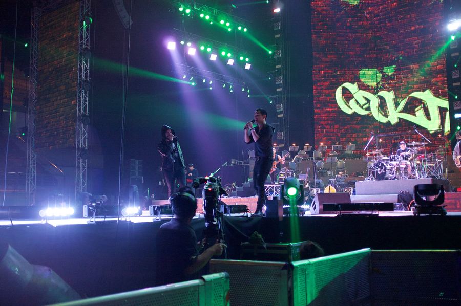 Band on a lit arena stage with an orchestra behind