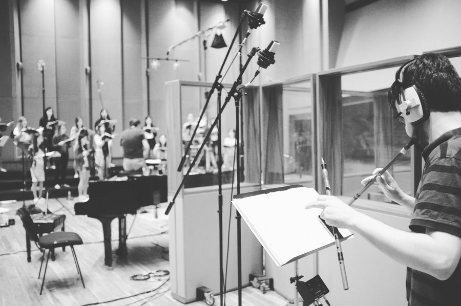 Flautist reading a part at a microphone, piano behind