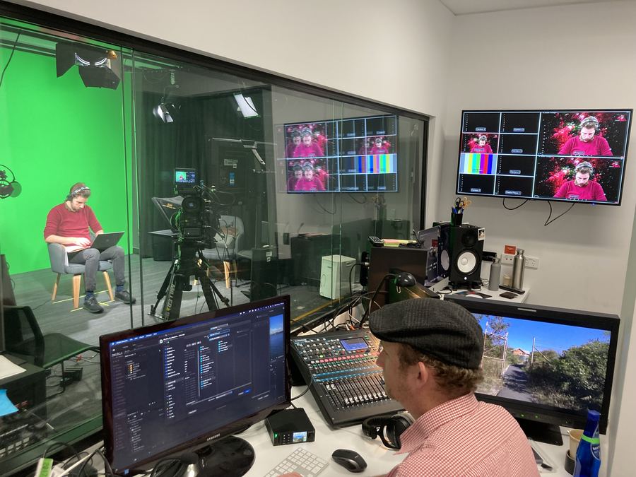Operator at a mixing desk beside a glass wall into a green-screen studio