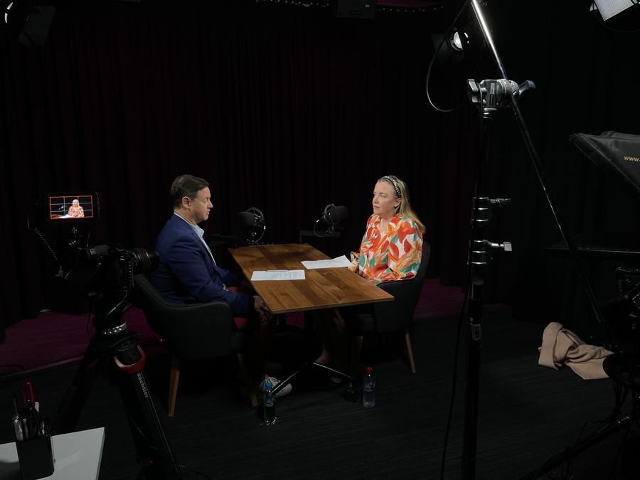 Two people talking across a table under studio lights