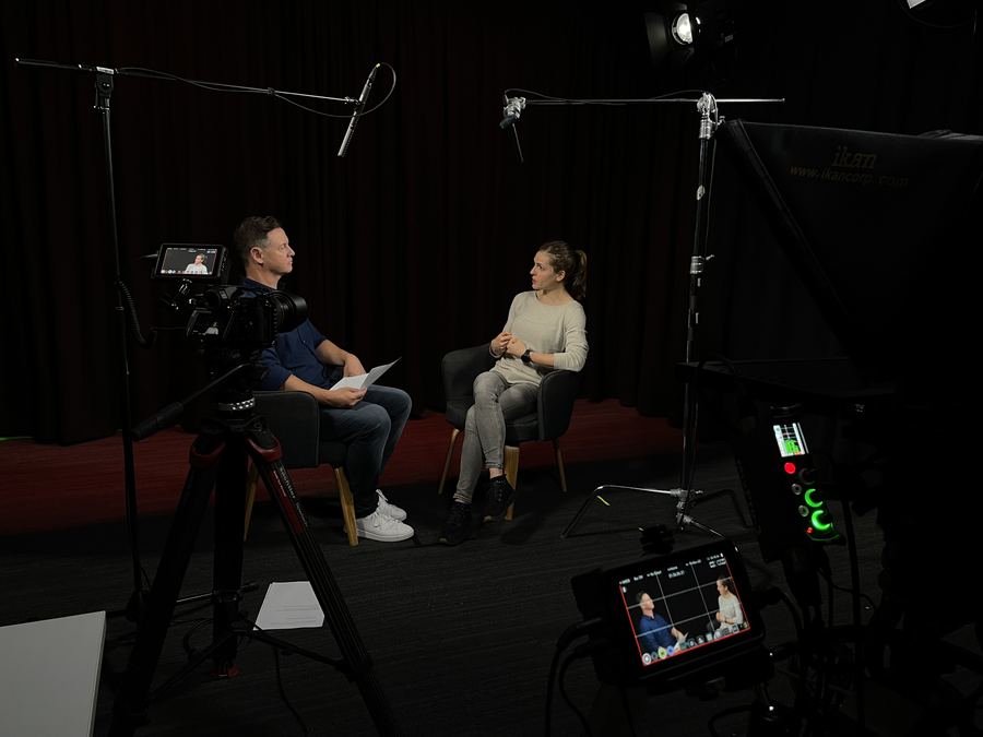 Two people seated for an interview, cameras and monitors framing the shot