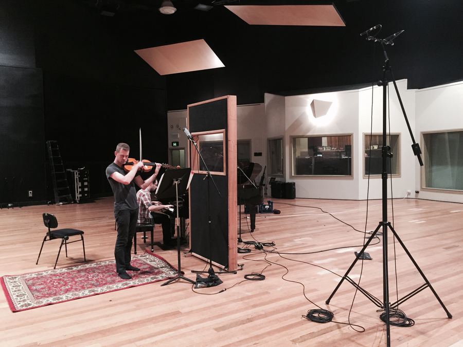 Violinist playing in a bright live room beside acoustic panels