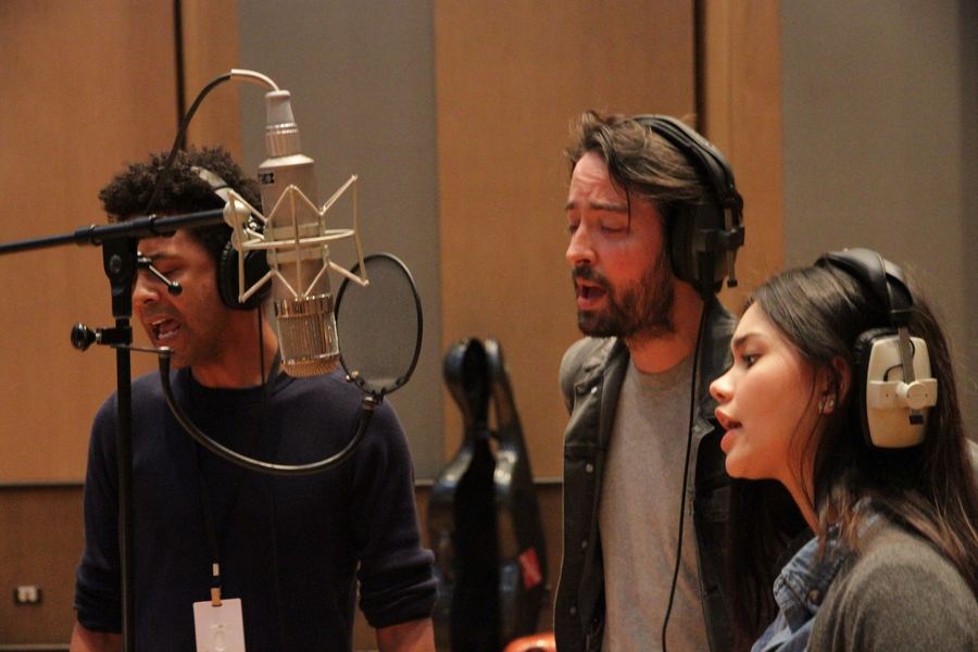 Three singers in headphones around a single microphone